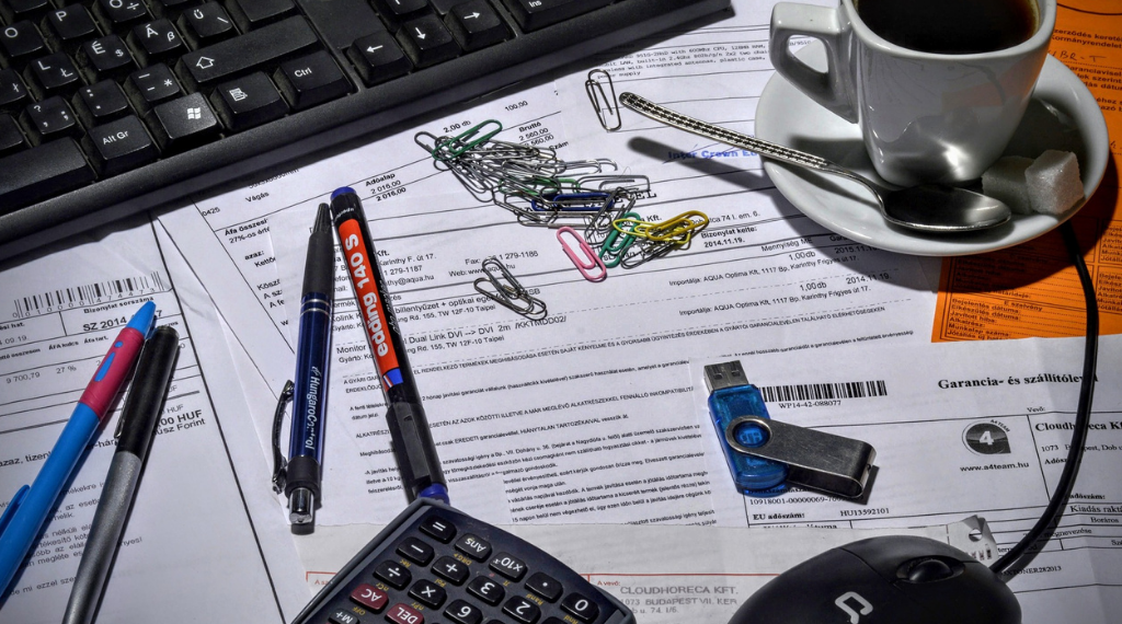 a messy desk of papers, USB drives and computers